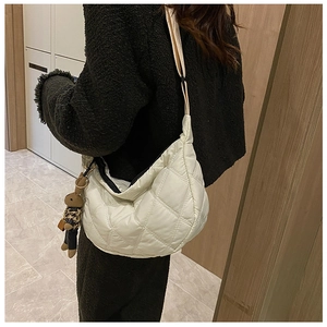 Side view of a white quilted crossbody dumpling bag with a brown plush rabbit charm