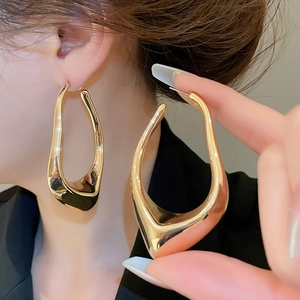 Macro detail of geometric irregular hollow earrings in glossy gold on model's ear