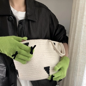 Close-up of green knitted bow gloves paired with a geometric patterned woven handbag