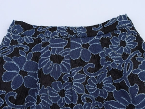 Detail of black lace trousers featuring blue denim floral embroidery and frayed edges