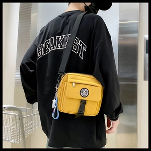 Detail of yellow canvas crossbody bag with black adjustable strap and buckle on streetwear