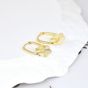 Elegant gold flower oval hoop earrings displayed on a white textured ceramic plate