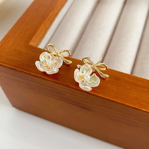 Macro detail of gold-plated flower stud earrings with a bow and shimmering pearl inlay