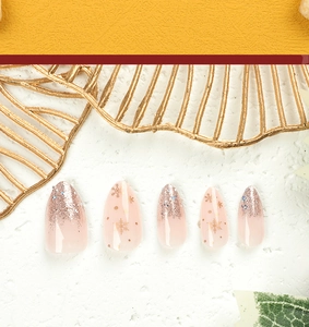 Macro detail of nude pink almond press-on nails with gold snowflakes and glitter gradient
