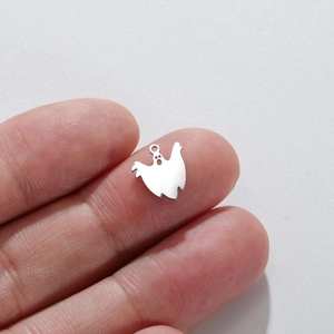 Close-up of a small polished stainless steel ghost charm held on a fingertip for scale