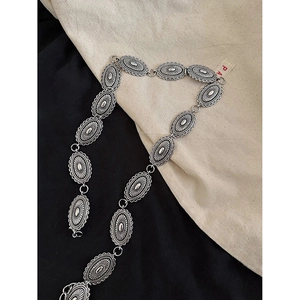 Détail d'une ceinture chaîne argentée avec maillons ovales et motifs feuilles en relief