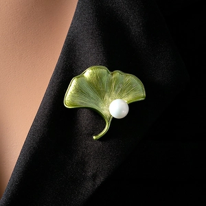 Detailed view of a green enamel ginkgo leaf brooch with a white pearl on a black suit