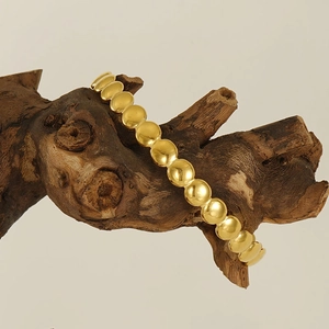 Polished golden stainless steel beaded bracelet on a natural wood stand