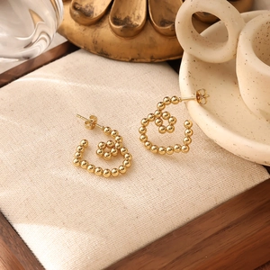 Detailed shot of 18K gold plated heart earrings on elegant beige linen cushions