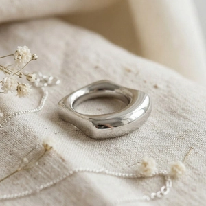 Minimalist silver irregular wave square stainless steel ring on beige linen with dried flowers
