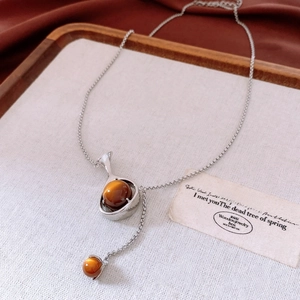 Détail d'un collier en Y argenté avec pierres oeil de tigre brunes et cadre goutte