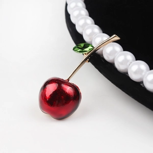 Detail of cherry brooch with red enamel finish and olive green crystal on gold metal