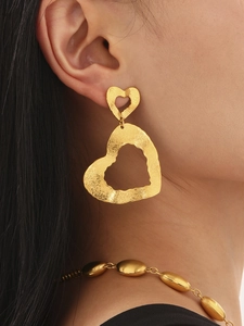 Detail van 18k gouden hartvormige oorbellen met gehamerde textuur en kralenketting op model
