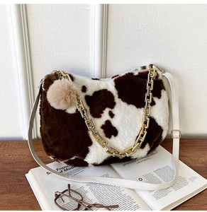 Detail of cow print faux fur tote bag with gold chain strap and plush ball charm