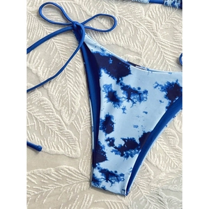Detail of blue and white tie-dye bikini bottoms with side string ties on textured background