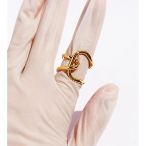Exaggerated irregular gold knotted wide band ring on a gloved hand with white background