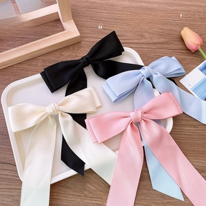 Detail shot of four satin bow hair clips in black, blue, cream and pink on a white tray