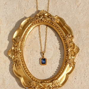 Detailed view of square blue gemstone pendant on a golden paperclip chain in a frame