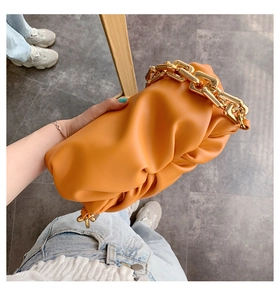 Macro shot of orange pleated cloud bag texture with bold gold chain handle detail