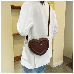 Dettaglio della piccola borsa a tracolla a forma di cuore marrone scuro indossata da modella