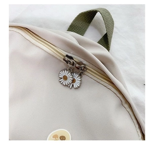 Detailed close-up of daisy zipper pulls on a beige canvas school backpack with green straps