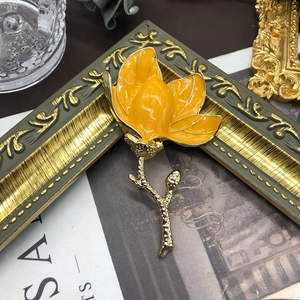Detail of elegant yellow enamel magnolia brooch on a vintage gold frame and antique paper