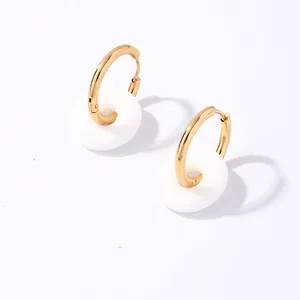 Détail de boucles d'oreilles dorées en acier inoxydable avec pendentifs ronds blancs