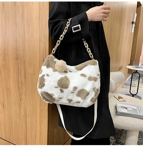 Detail of plush cow print tote bag with golden metal chain and soft fur ball charm