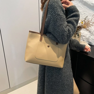 Minimalist large khaki tote bag with dark brown trim shown in a lifestyle commuter setting