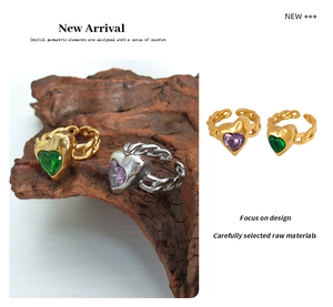 Detail of gold and silver heart rings featuring green and purple crystals on cuban link bands
