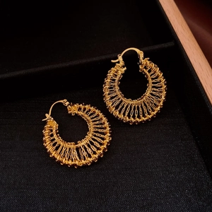 Detail of gold plated hollow woven hoop earrings on a black textured display plate