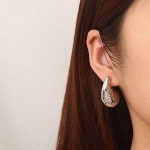 Detail view of a silver teardrop earring with hammered texture worn on a model's ear