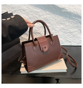 Detail of dark brown faux leather handbag with crocodile pattern and square clasp closure