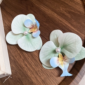 Detailed close-up of floral hair clips with pearls and gradient green petals on wood