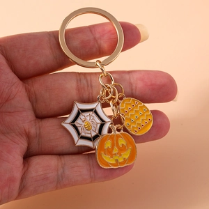 Detail of Halloween keychain with enamel pumpkin and spider web charms held in hand