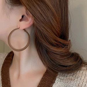 Detail view of a large dark brown flocked geometric hoop earring on a female model