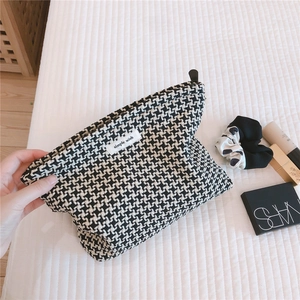 Close-up of black and white houndstooth cosmetic bag with simple wish label and zipper