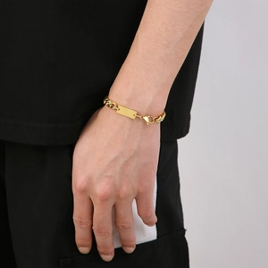 Close-up of gold tone Cuban link chain bracelet with blank rectangle bar on wrist