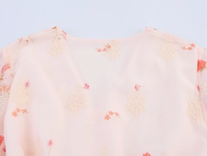 Détail de la broderie florale et bouton perle sur l'encolure de la robe rose clair