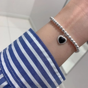 Close-up of beaded bracelet with black heart pendant worn on a female wrist