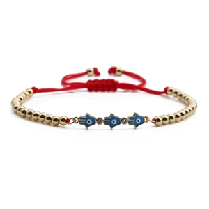 Macro shot of Hamsa Hand charms and red woven cord on an adjustable beaded bracelet