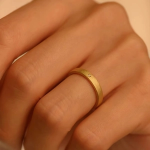 Detail of 18k gold matte ring featuring a starburst-set zircon on woman's finger