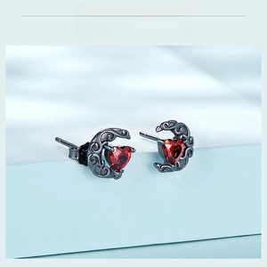 Detail of vintage moon stud earrings featuring red heart gems and ornate silver patterns