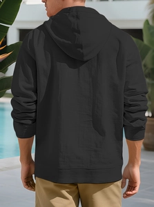 Rear view of man in black hooded linen shirt by an outdoor pool, casual beach style