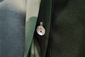 Détail d'un bouton en nacre sur le tissu satiné à imprimé floral vert de la blouse