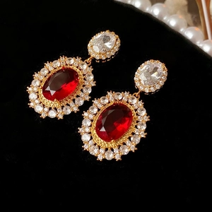 Dettaglio orecchini ovali dorati vintage con grande zircone rosso e pavé di pietre