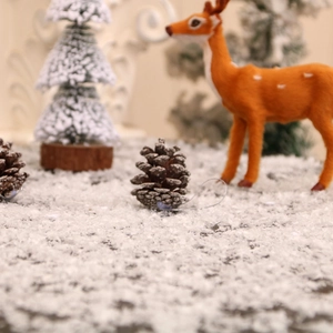 Close-up of pine cone ornaments on artificial snow with a festive Christmas tree backdrop