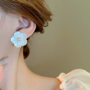 Close-up of elegant shell flower stud earring with a central pearl on model's ear