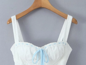 Detailansicht eines weißen Spitzentops mit hellblauer Bandschleife und Stickereiverzierungen