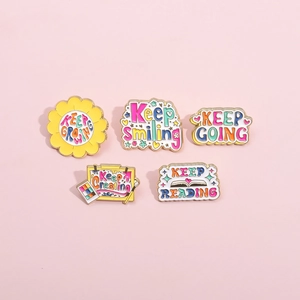 Set of five colorful enamel pins with motivational quotes like Keep Growing on pink background